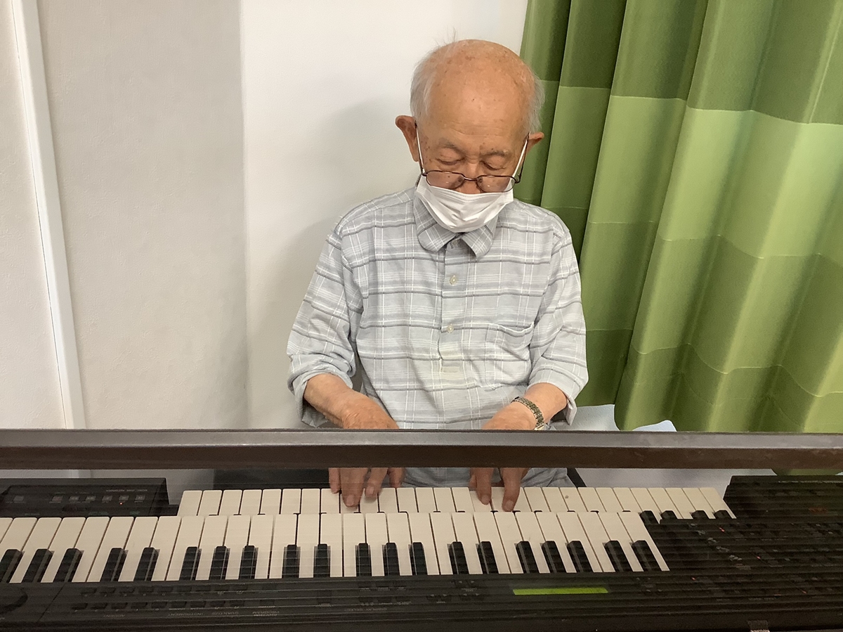 高齢入居者がキーボードを演奏している。音楽レクリエーション活動の様子。